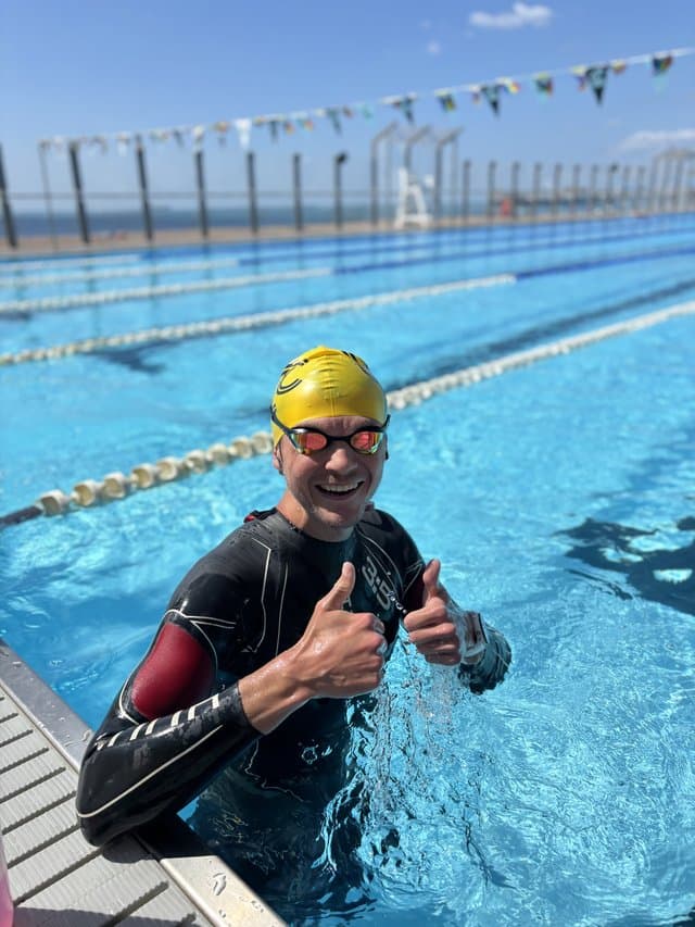 A swimmer in a wetsuit at the wall, giving a thumbs up mid-set